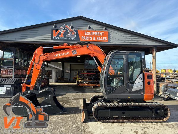 En orange och grå Hitachi-grävmaskin parkerad framför en verkstad.