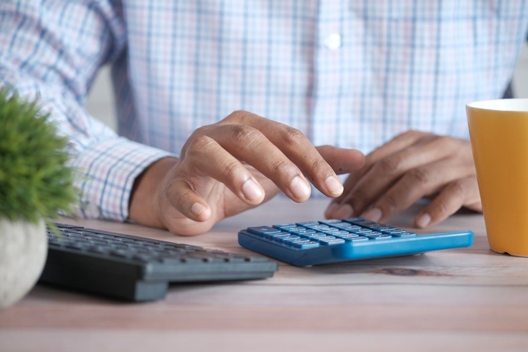 Person använder en blå miniräknare vid ett skrivbord