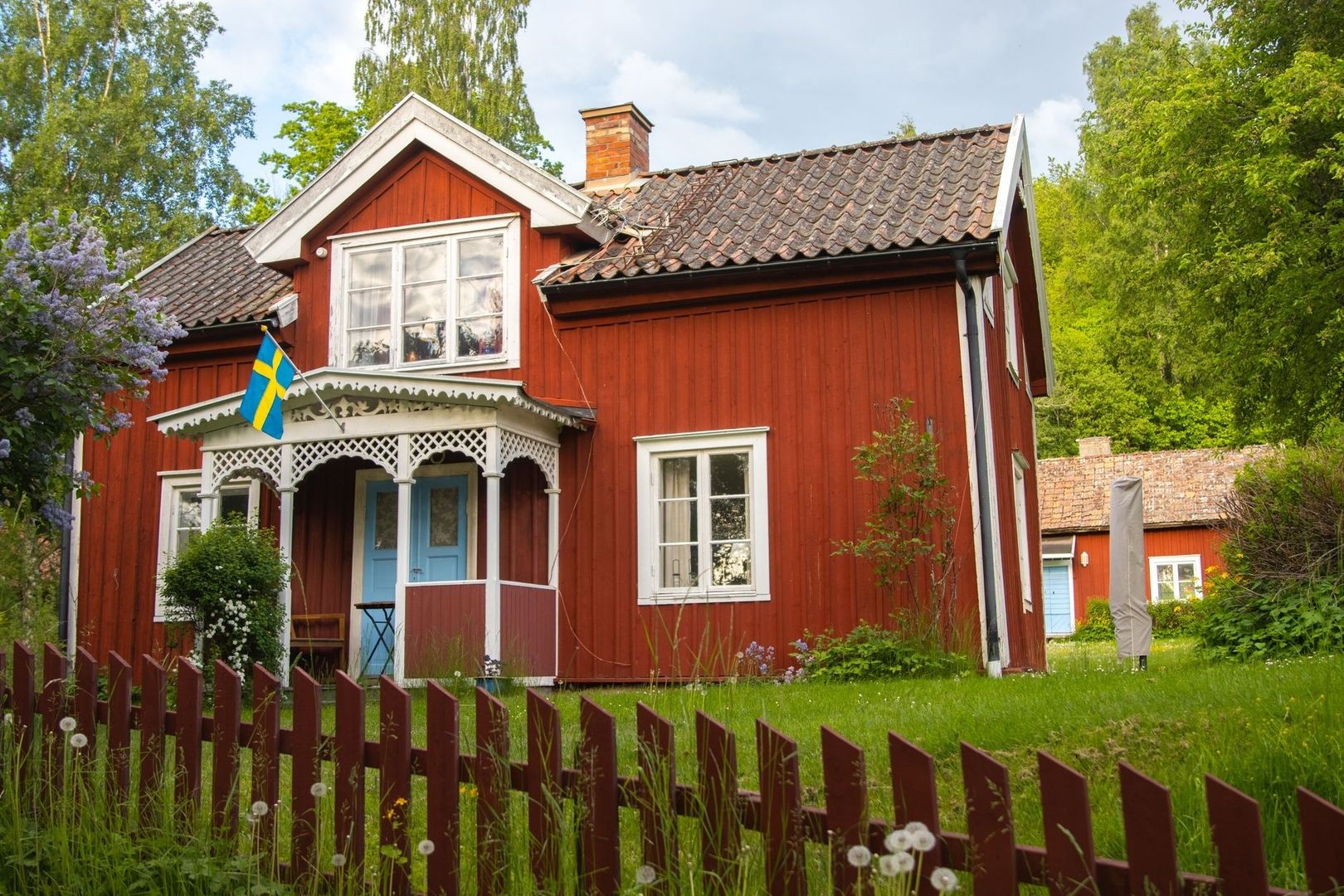 Faluröd trästuga med snickarglädje, blå dörr och svensk flagga